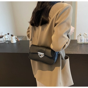 Détail d'un sac bandoulière en cuir noir avec une boucle métallique triangulaire argentée