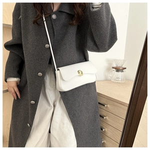 Detail of a minimalist white leather crossbody bag featuring a gold circular floral metal lock