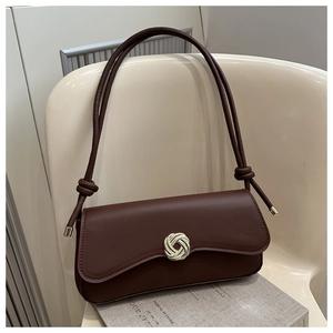 Detail of chocolate brown underarm bag featuring a silver knot buckle on a minimalist chair