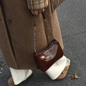 Close-up of a glossy dark brown baguette bag with metal chain strap on a wool coat