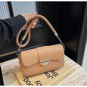 Détail d'un sac bandoulière beige avec fermoir bouclier argenté et poignée en cuir sur un livre