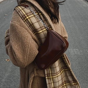 Detail of dark brown glossy leather hobo bag with silver chain strap on wool coat