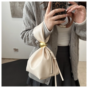 Detail of cream pleated bucket bag featuring golden spherical buckle and soft leather texture