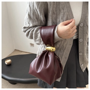 Close-up of a burgundy pleated bucket bag with a stylish gold metallic sphere handle