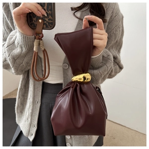 Detail of burgundy pleated bucket bag with a large polished gold metal bead on the handle
