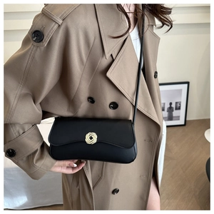 Detail of black leather shoulder bag with a gold interlocking floral buckle on a beige coat