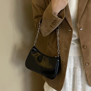 Detail of minimalist black patent baguette bag with silver chain strap on model