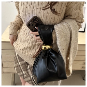 Detail of black pleated bucket bag featuring chunky gold metal ring handle and leather strap