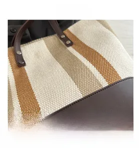 Detail view of woven canvas tote bag with brown leather handles and vertical stripes