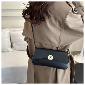 Detail of a black rectangular crossbody bag with a golden round metal buckle on a trench coat