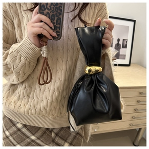 Detail of black pleated bucket bag featuring a decorative gold metallic knot clasp