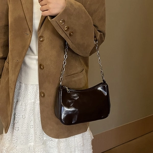 Detail of glossy brown underarm bag with silver chain strap worn with dark brown suit