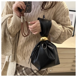 Detail of black pleated bucket bag featuring a polished gold metal ball and leather drawstrings
