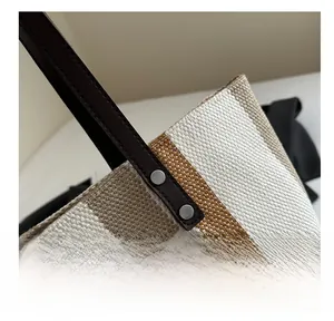 Detail of woven tote bag with brown leather handles and silver metal rivet reinforcement