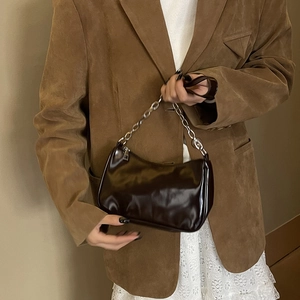 Close-up of a dark brown glossy patent leather shoulder bag with a silver metal chain handle