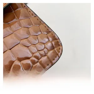Macro detail of brown crocodile embossed leather texture and stitching on square bag