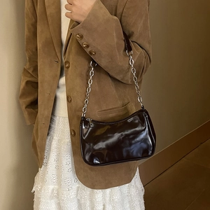 Detail of dark brown patent leather underarm bag with silver chain strap on a model
