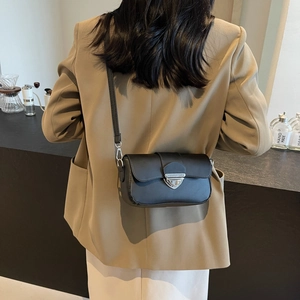 Sac bandoulière noir chic avec boucle argentée porté par un mannequin dans un café