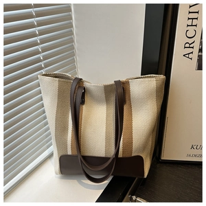 Close-up of a striped canvas tote bag with brown leather handles and textured knitting