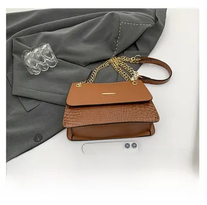 Brown faux leather shoulder bag with crocodile texture next to a smartphone for scale
