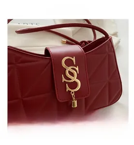 Macro shot of red quilted faux leather shoulder bag with gold hardware logo and tassel