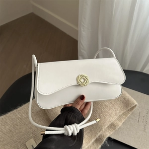 White leather shoulder bag with gold knot buckle held against a minimalist background