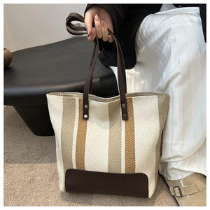 Close-up of striped canvas tote bag showing leather handles and silver rivet details