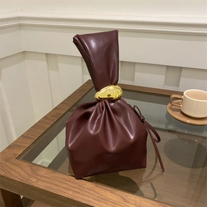 Vintage burgundy pleated bucket bag with gold metal ring detail on a wooden table