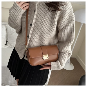 Detail view of brown PU leather shoulder bag with a gold metal buckle on a beige cardigan