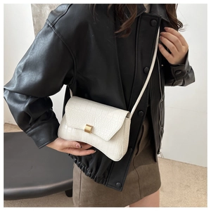 Détail du sac blanc à motif crocodile avec boucle dorée sur une veste en cuir noir