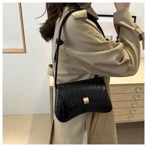 Détail d'un sac à bandoulière noir motif crocodile avec boucle dorée et nœud décoratif