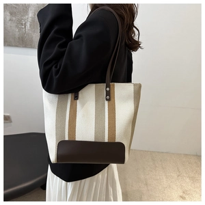Canvas tote bag with striped pattern and leather handles worn by a model in a suit