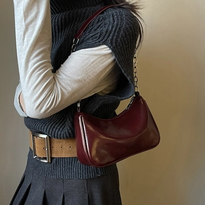 Detail of burgundy glossy leather underarm bag with chain strap on model's shoulder