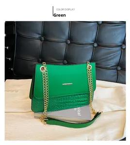 Detail of green shoulder bag with crocodile pattern and golden metal chains on white fabric
