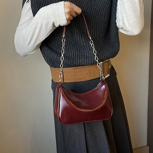 Glossy burgundy shoulder bag with metallic chain detail and leather strap shown on a model