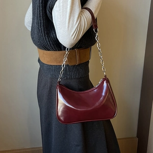 Detail of dark burgundy patent leather underarm bag with chunky silver chain and strap