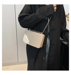 Close-up of golden sequin crossbody chain bag worn with a stylish black coat