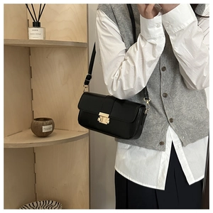 Detail of a black leather underarm bag featuring a square gold metal clasp and thin strap