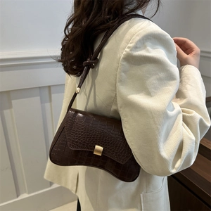 Sac sous le bras marron à motif crocodile avec fermoir doré porté par un mannequin