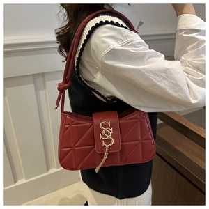 Close-up of red quilted shoulder bag with gold metal logo and tassel detail on leather strap