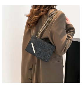 Detail of black sequin crossbody bag with gold chain strap worn over a brown suit