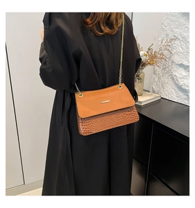 Detail of a brown leather shoulder bag with crocodile texture and gold chain strap
