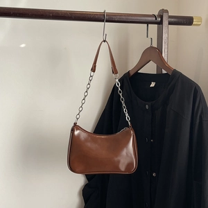 Detail of a brown glossy leather shoulder bag featuring a silver metal chain and zipper