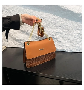 Detail of a brown shoulder bag featuring crocodile pattern texture and golden chain strap