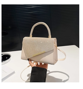 Detail of beige rhinestone-encrusted flap bag with golden metal handle and PU leather