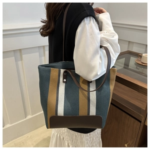 Detail of striped canvas tote with brown leather handles and silver rivet reinforcement