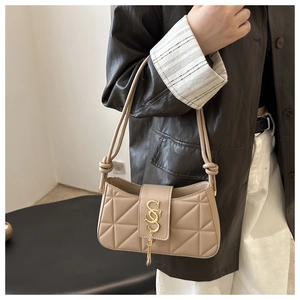 Detail of beige quilted shoulder bag with golden S-buckle and tassel pendant on a model
