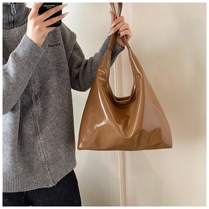 Detail of glossy brown patent leather tote bag with wide shoulder strap design