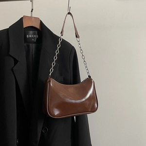 Close-up of brown glossy leather underarm bag with silver chain strap on a blazer