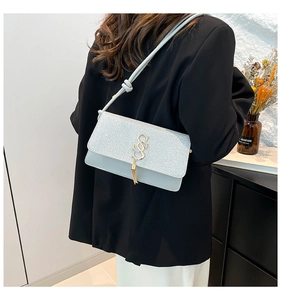 Détail du sac en cuir bleu à paillettes argentées, logo SS doré et pompon à franges